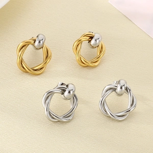 Detail of twisted metal hoop earrings in gold and silver finishes on textured fabric