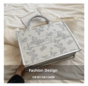 Close-up of silver tote bag featuring butterfly embroidery and structured top handles