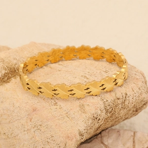 Brazalete de acero inoxidable dorado con diseño de hojas sobre fondo de piedra