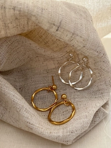 Macro shot of minimalist gold and silver round fringe earrings on natural linen