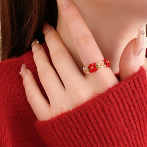 Close-up of model wearing a red and transparent handmade beaded flower ring with knitwear