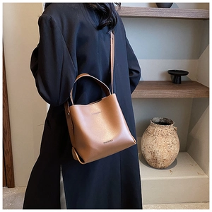 Brown leather bucket bag shown as a shoulder bag on model in a warm interior setting