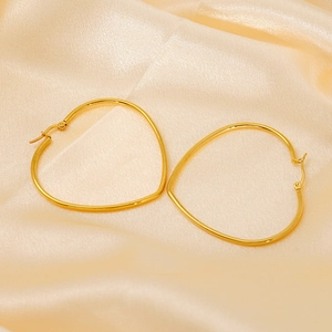 Boucles d'oreilles créoles cœur en acier titane doré sur un tissu en soie beige