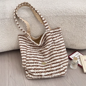 Detail view of a striped plush tote bag featuring a textured finish and metal logo plaque