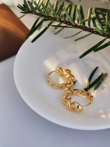 Detailed close-up of golden twisted rope hoop earrings on a white porcelain tray