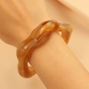 Macro shot of an amber resin cuff bracelet with irregular wave design on a woman's wrist