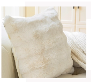 Close-up of a white plush square pillowcase on a beige sofa with a soft knit blanket