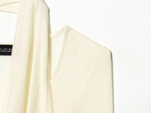 Detail of cream white knit shirt neckline and shoulder with fabric care label view
