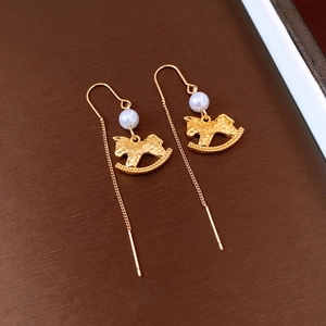 Detailed view of gold rocking horse earrings with pearls and long chain on a dark background
