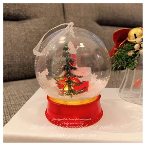 Close-up of lighted Christmas snow globe featuring a miniature tree and red house decoration