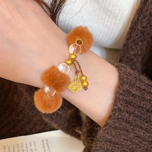 Gros plan d'un bracelet d'hiver avec pompons marrons, perles et un pendentif fleur dorée