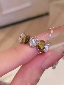 Close-up of a silver ring with three zircon stones and two oval tiger eye stones on a finger