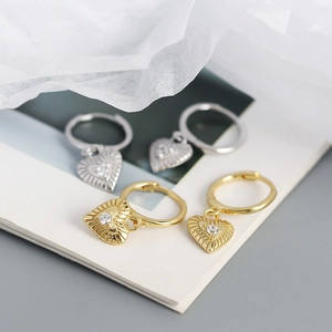 Detailed close-up of heart-shaped earrings with central zircon in gold and silver