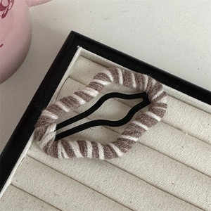 Detailed shot of a cloud-shaped brown and white striped knit BB hair clip on a jewelry tray