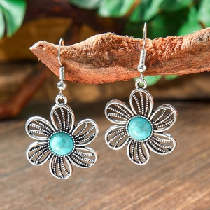 Macro shot of silver filigree flower earrings with turquoise stone on a wooden branch