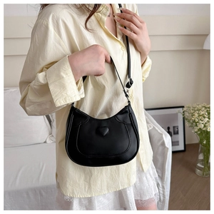Model wearing a black crescent-shaped shoulder bag with 3D heart-shaped indentation