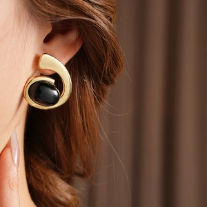 Close-up of golden swirl earring with a large black oval gemstone on model