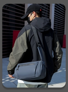 Side view of blue-grey waterproof crossbody bag worn by model against modern building