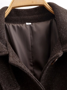 Detailed view of dark brown wool coat collar and shoulder texture on wooden hanger
