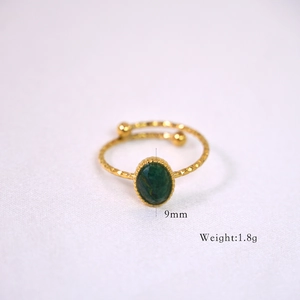 Macro detail of gold-plated ring featuring green oval gemstone with hammered metal texture