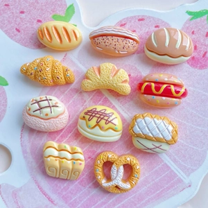 Flat lay of 11 miniature resin assorted bread and pastry charms on a pink background