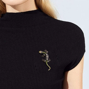 Vintage lizard brooch with white gems and green accents on a black knit background