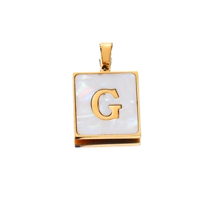 Macro detail of square gold-plated pendant with white shell inlay and letter G design