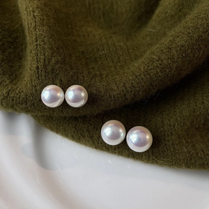 Macro view of white round pearl earrings with iridescent luster on a knit fabric and ceramic