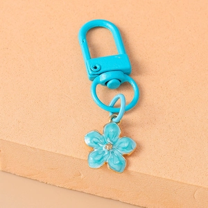 Detail of blue flower keychain with gold edges and rotatable metal hook on beige foam