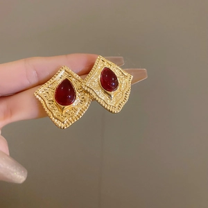 Close-up of vintage gold earrings with textured diamond shape and teardrop red gemstone