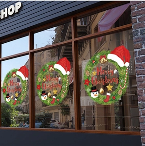 Detailed Christmas wreath window stickers with snowmen and gold bells on a shop glass
