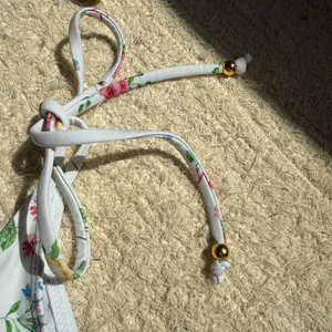 Detail view of floral bikini straps with decorative gold sphere charms and pink rose print