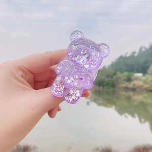 Detail of purple glitter bear phone grip stand held against a scenic lake background