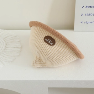 Detailed view of the thick vertical knit texture and brown leather label on the beige beanie