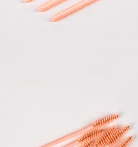Macro shot of disposable mascara wands with pink-orange handles and bright orange spiral bristles