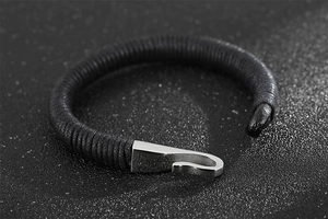 Detailed close-up of a black braided leather bracelet with a silver metal fish hook clasp