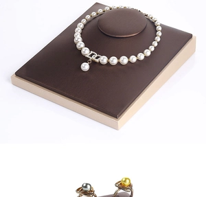 Detail view of pearl necklace with gold CD pendant and rings on dark jewelry stand