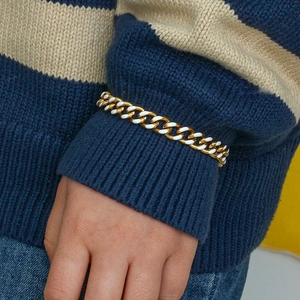 Detail of a gold Cuban link bracelet with white enamel on a striped sweater sleeve