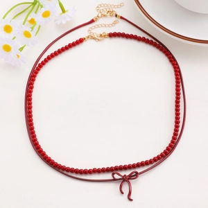 Detail of red beaded necklace and cord chain with a shiny bow pendant and gold clasp