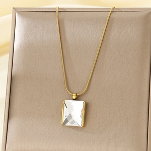 Close-up of a square clear crystal pendant on a gold snake chain over a soft fabric base