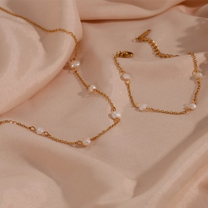 Close-up of gold chain necklace and bracelet with white pearls on pink silk fabric