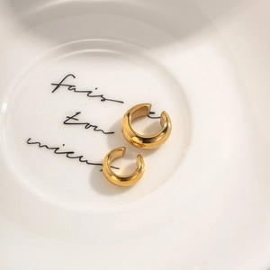 Minimalist C-shaped gold stainless steel hoop earrings on a decorative ceramic dish