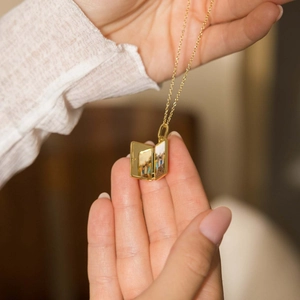 Detail of hand holding a golden book locket necklace that opens to hold personal photos