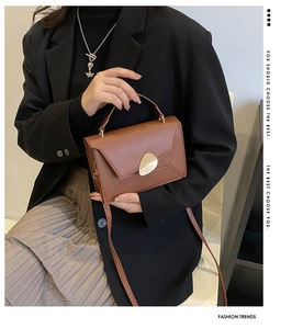 Detail of tan rectangular crossbody bag with golden oval buckle and envelope flap cover