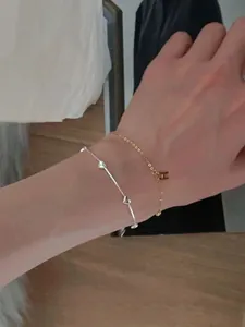 Close-up of S925 silver heart bracelet and gold H pendant chain layered on wrist