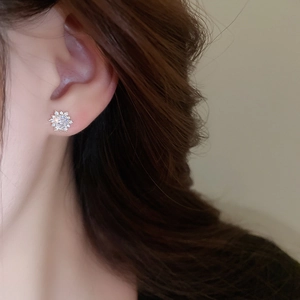 Close-up of minimalist zircon snowflake stud earrings on a model's earlobe