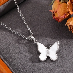 Close-up of silver bow pendant with pearl shell wings and diamonds on a grey jewelry box