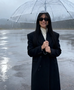 Detail of a chic black pinstripe long coat styled with a white turtleneck and umbrella