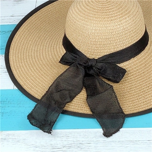 Close-up of straw sun hat with black mesh ribbon bow and edge detailing on wooden surface