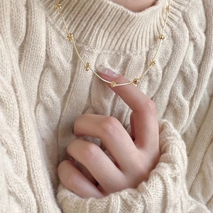 Close-up of golden beaded silver necklace worn on a cream knit sweater background